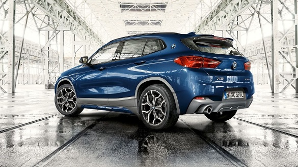 Blauer BMW X2 in hellem, industriellem Raum, Rückansicht, auf Schienen stehend.