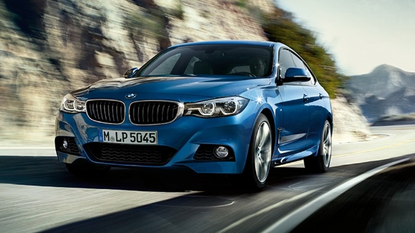 Blauer BMW auf kurviger Straße, umgeben von Felsen und Himmel im Hintergrund.