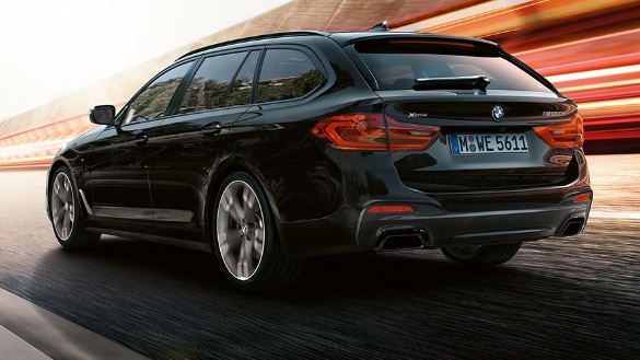 Schwarzer BMW Touring von hinten, fährt auf einer Straße, unscharfer Hintergrund.