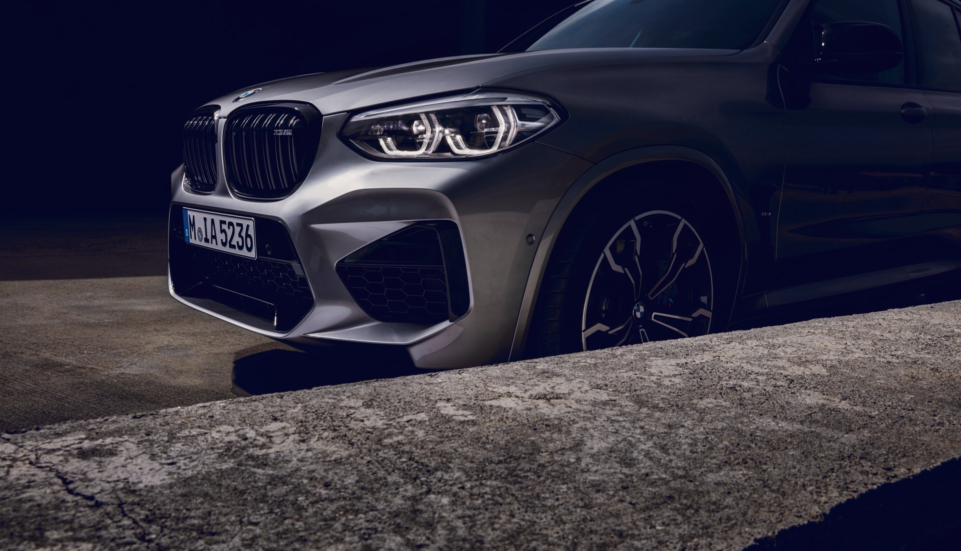Frontansicht eines silbernen BMW X3 M auf dunklem Hintergrund.