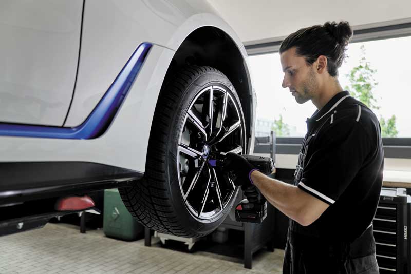 Person wechselt Reifen an einem weißen Auto in einer Werkstatt.