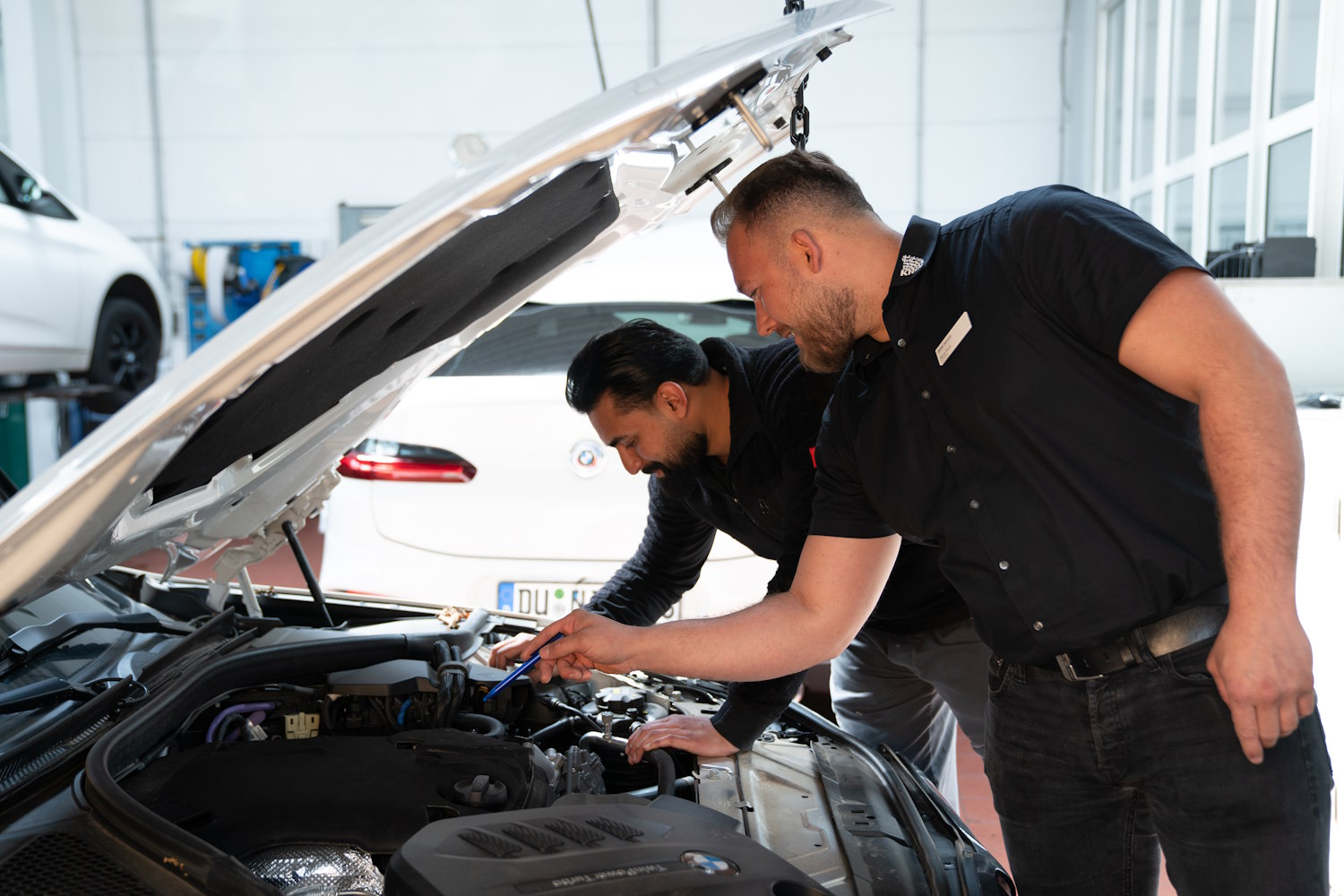 Zwei Männer inspizieren den Motor eines Autos in einer Werkstatt.