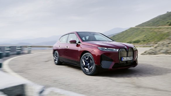 Ein roter BMW iX fährt auf einer kurvigen Straße in einer bergigen Landschaft.