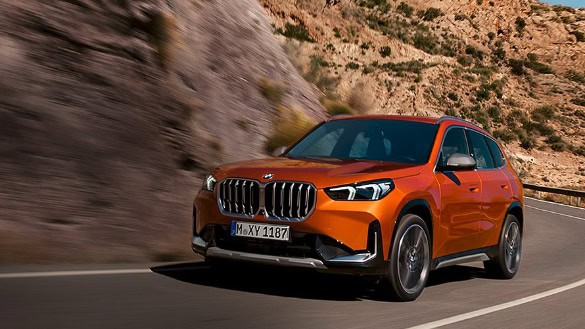 Oranger BMW X1 fährt auf einer kurvigen Straße durch eine felsige Landschaft.