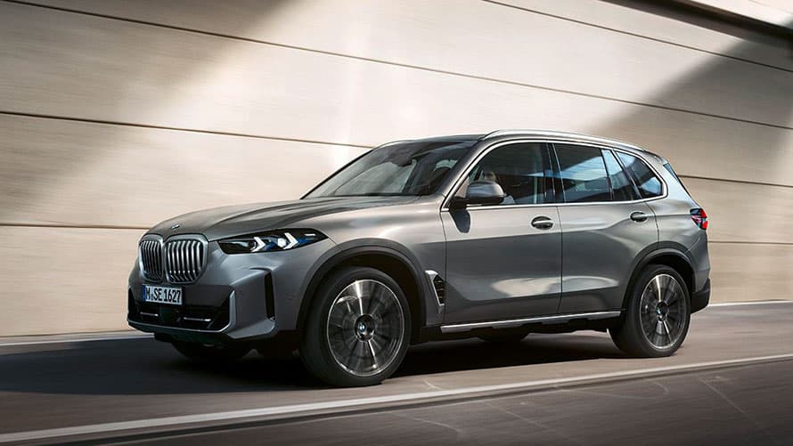 Silberner BMW X5 fährt vor beiger Wand; Seitenansicht; modernes Design.