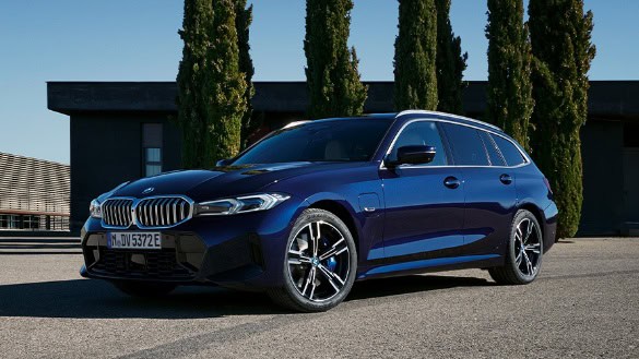 Blauer BMW Kombi auf Parkplatz, umgeben von Zypressen und einem modernen Gebäude im Hintergrund.