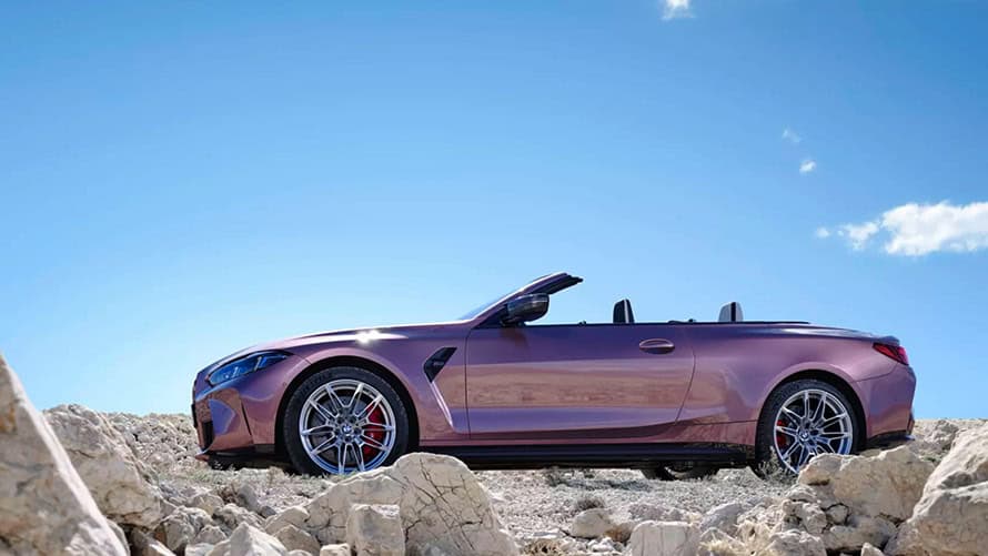Lila BMW Cabrio auf felsigem Gelände vor blauem Himmel, seitlich aufgenommen.