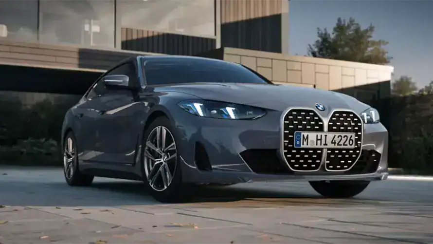 Graues BMW 4er Gran Coupé auf gepflastertem Platz vor modernem Gebäude bei Tag.