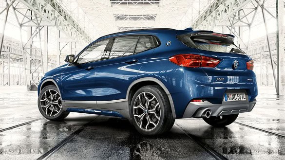 Blauer BMW X2 in einem hellen, industriellen Raum von hinten links fotografiert.