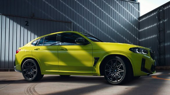 Grüner BMW X4 M steht seitlich in einem Industriehof mit Wellblechwand im Hintergrund.