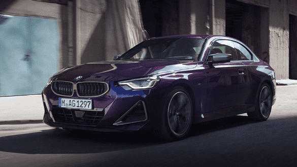 Rotes BMW Coupé fährt auf einer Straße, Stadt und Stromleitungen im Hintergrund.