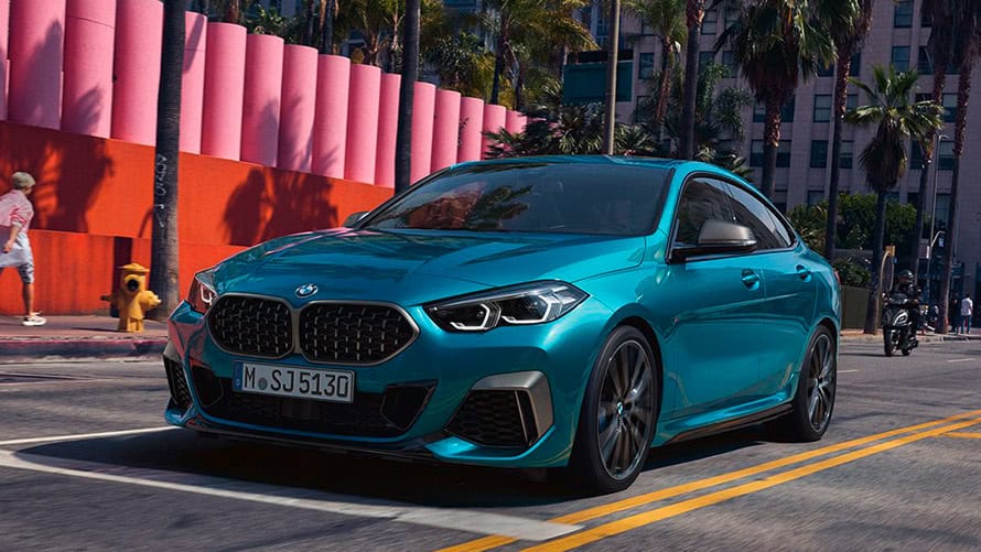 Blaues BMW Coupé fährt auf einer Straße, im Hintergrund Palmen und ein pinker Zaun.