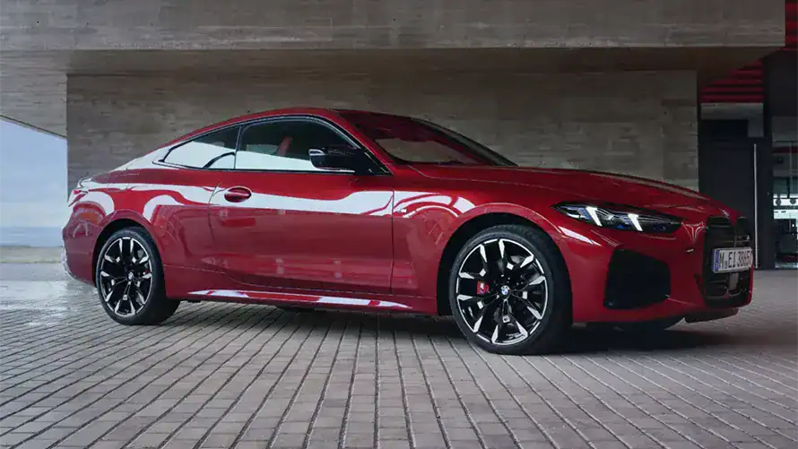 Rotes BMW 4er Coupé auf gepflasterter Fläche vor Betonwand, seitliche Ansicht.