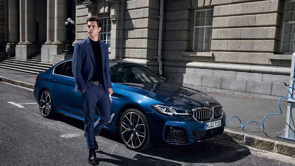 Blauer BMW 5er Limousine steht vor einem historischen Gebäude, Mann in Anzug lehnt am Auto.