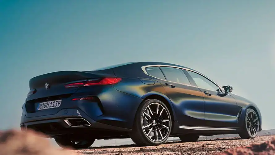 Blaues BMW 8er Gran Coupé, seitliche Ansicht, steht auf sandigem Boden unter klarem Himmel.