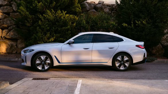 Weißes Auto in Seitenansicht auf einer Straße, im Hintergrund Bäume und Felsen.