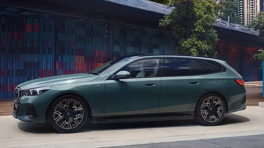 Grüner BMW Touring Kombi vor moderner Architektur und Bäumen.