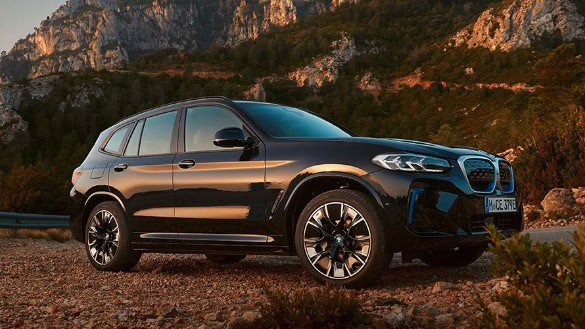 Weißer BMW-SUV steht vor einem Gebäude, an eine Ladestation angeschlossen.