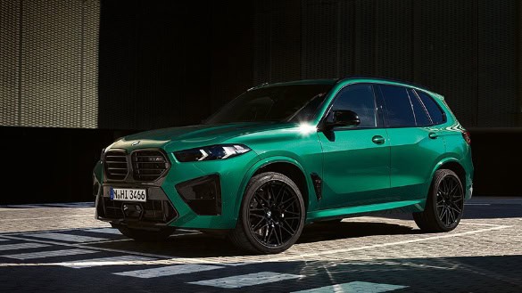Grüner BMW X5M auf gepflastertem Platz, seitliche Ansicht, im Hintergrund dunkle Wand.