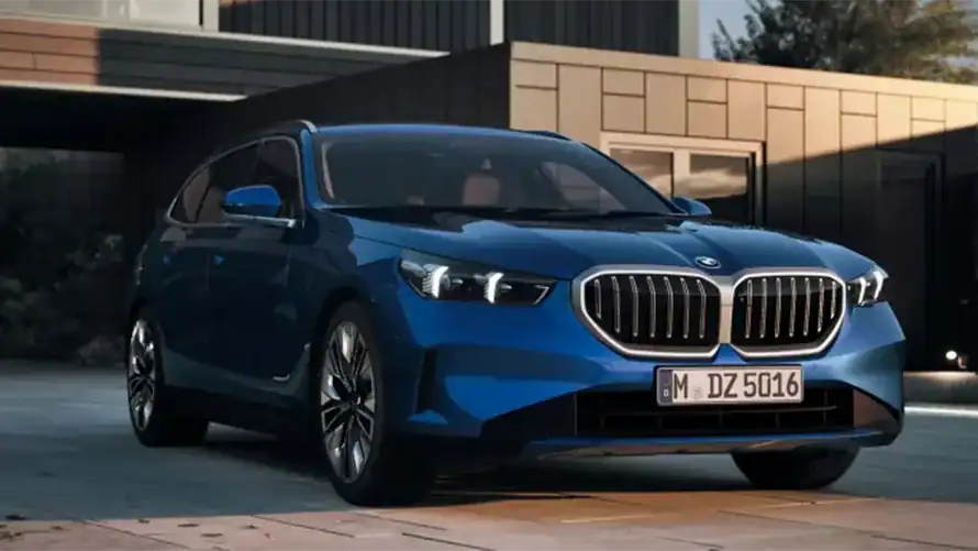 Blauer BMW 5er Touring 2024 steht vor einem modernen Gebäude bei Sonnenuntergang.