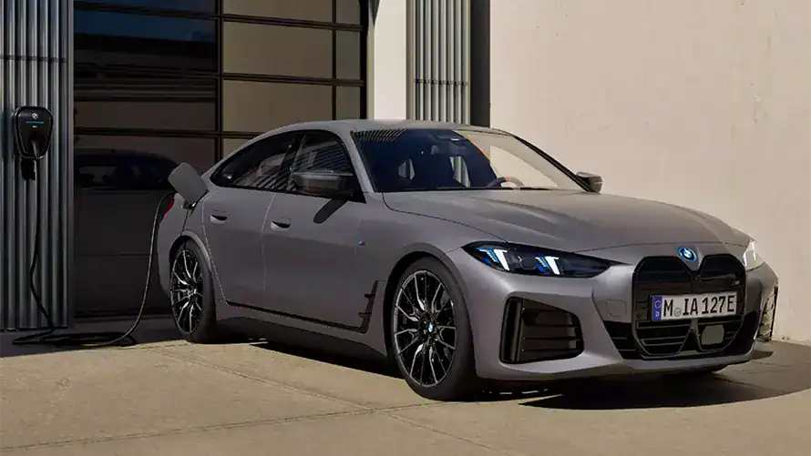 Grauer BMW i4 M50 lädt an einer Wandladestation im Freien.