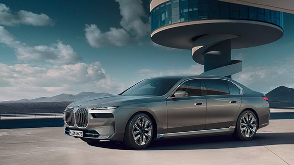 Silberner BMW i7 steht vor modernem Gebäude mit spiralförmigem Turm bei bewölktem Himmel.