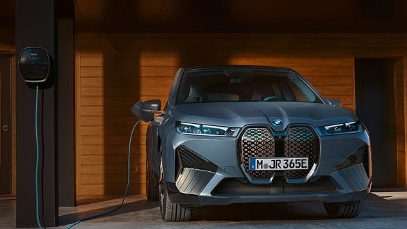 Grauer BMW iX M60 lädt an einer Ladestation in einer Holzgarage.