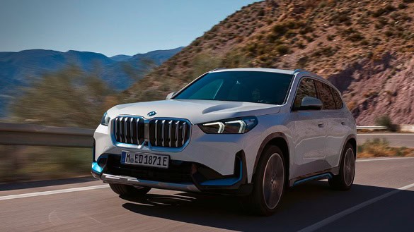Weißer BMW SUV auf einer Straße vor bergiger Landschaft.