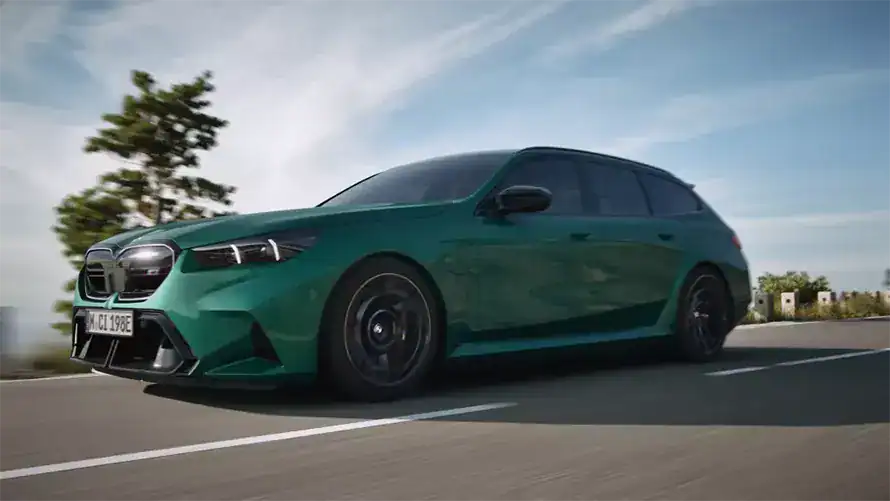 Grüner BMW-Kombi auf Straße, blauer Himmel, Bäume im Hintergrund.