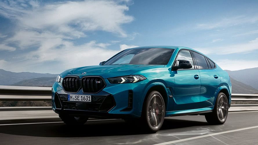 Türkiser BMW X6 fährt auf einer Straße, blauer Himmel im Hintergrund.