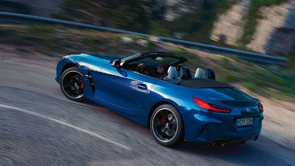 Blauer BMW Z4 Cabrio fährt auf kurviger Straße, dynamisch aus seitlicher Perspektive fotografiert.