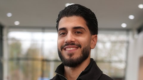 Eine lächelnde Person vor einem unscharfen Auto in einer Werkstatt.