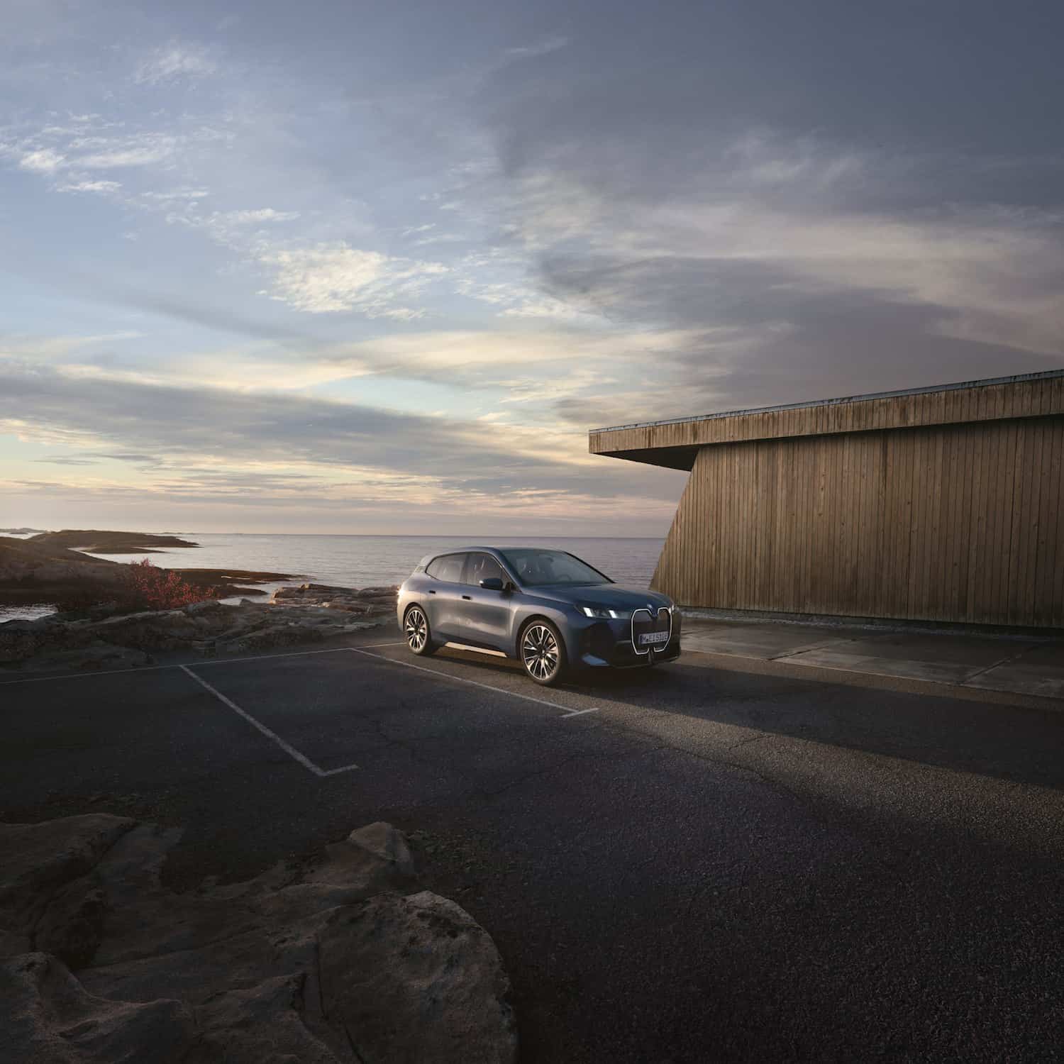 Roter BMW SUV steht bei Sonnenuntergang an einer Küste mit Meer im Hintergrund.